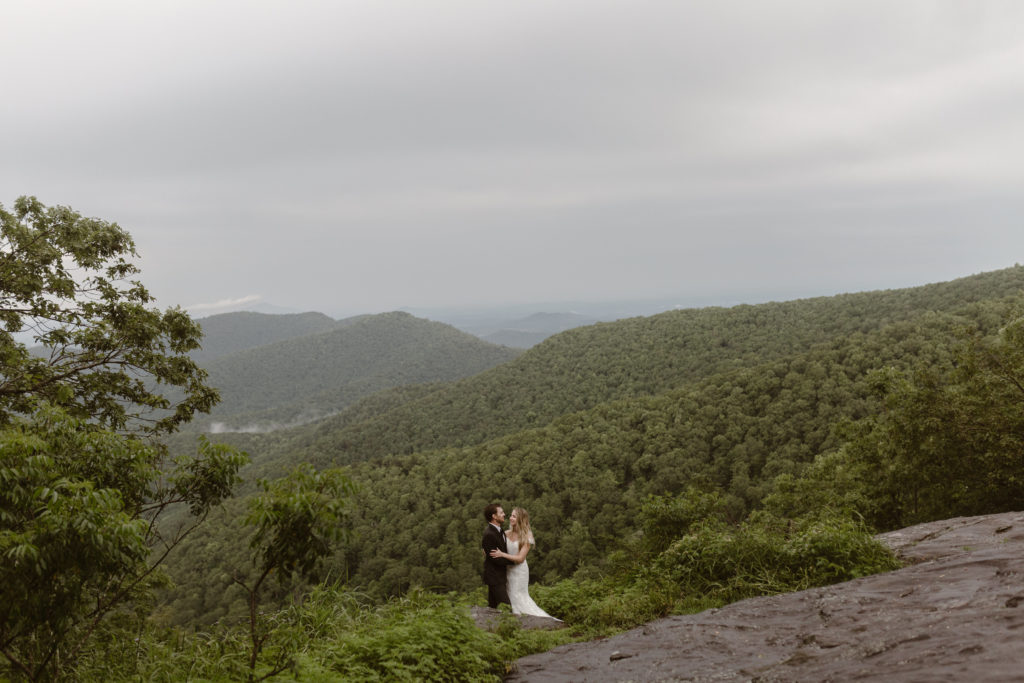 A bride and groom hugging each other with a mountain vista as the backdrop. 