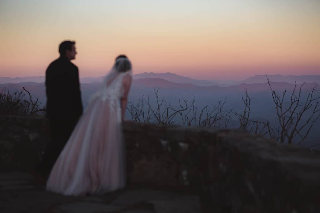 A bride and groom enjoys the colors of sunset on the mountain tops in the distance. 