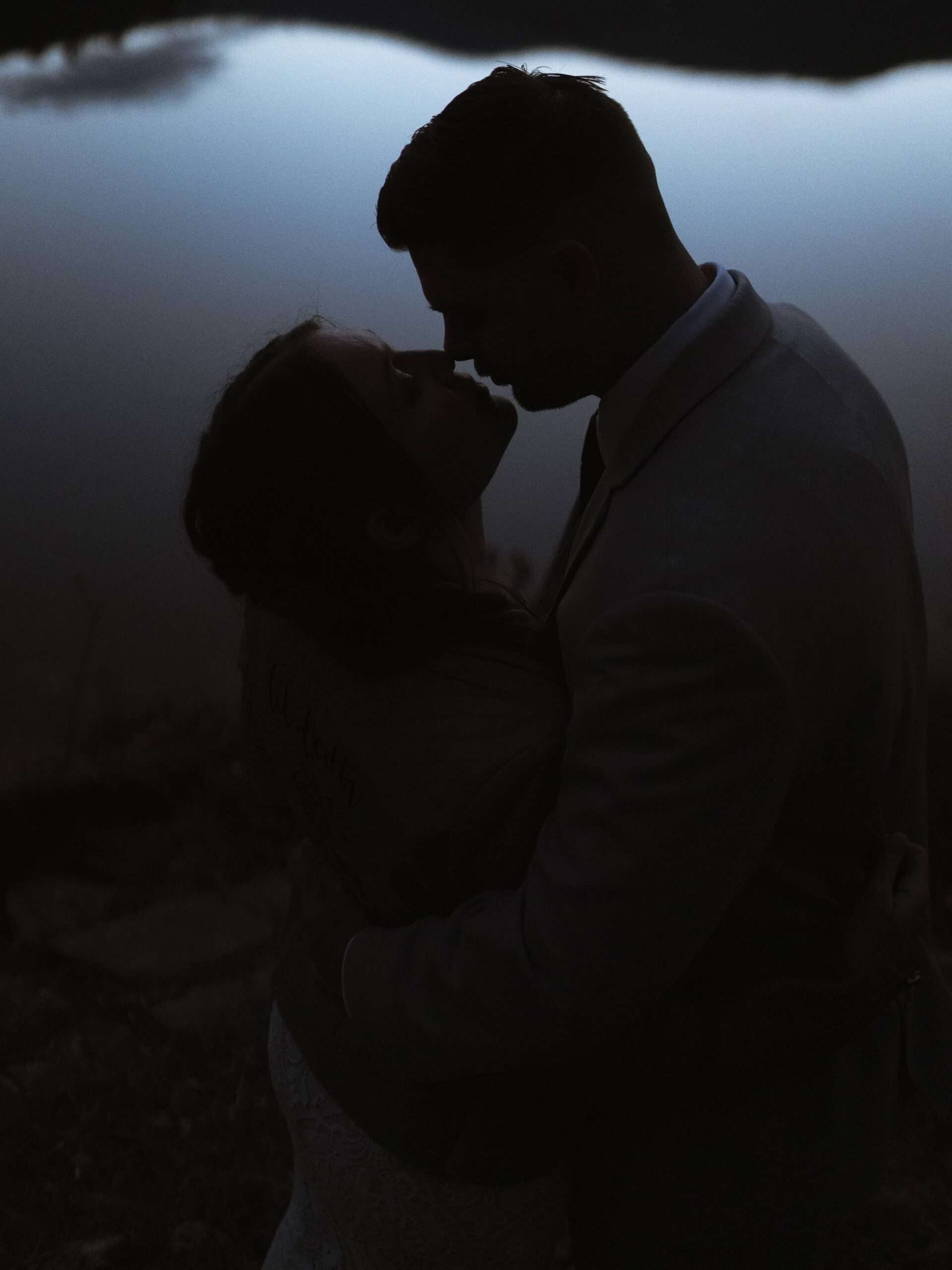 A silhouetted bride and groom going in for a kiss at dusk. 