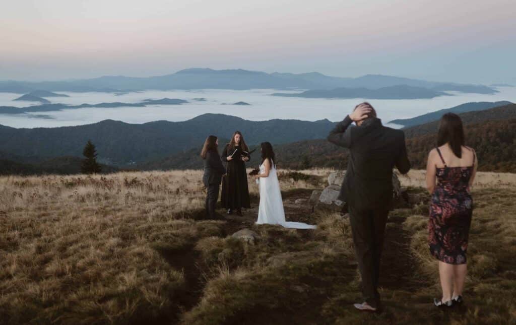 A wedding ceremony with bride, groom, two friends and officiant on top of a mountain with a cloud inversion.
