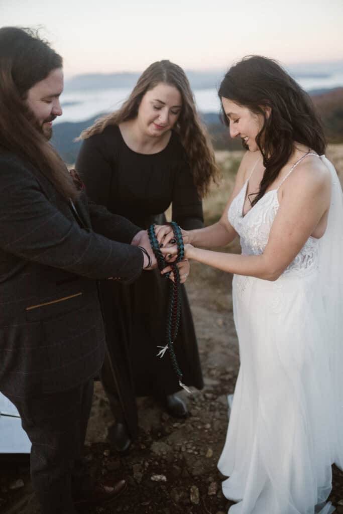 An officiant tying a bride and groom's hands together for a handfasting ceremony. 