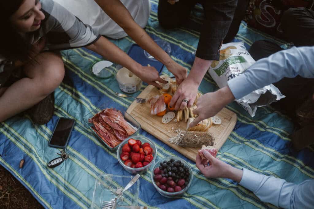 Friends enjoying a charcuterie board on a picnic blanket. 