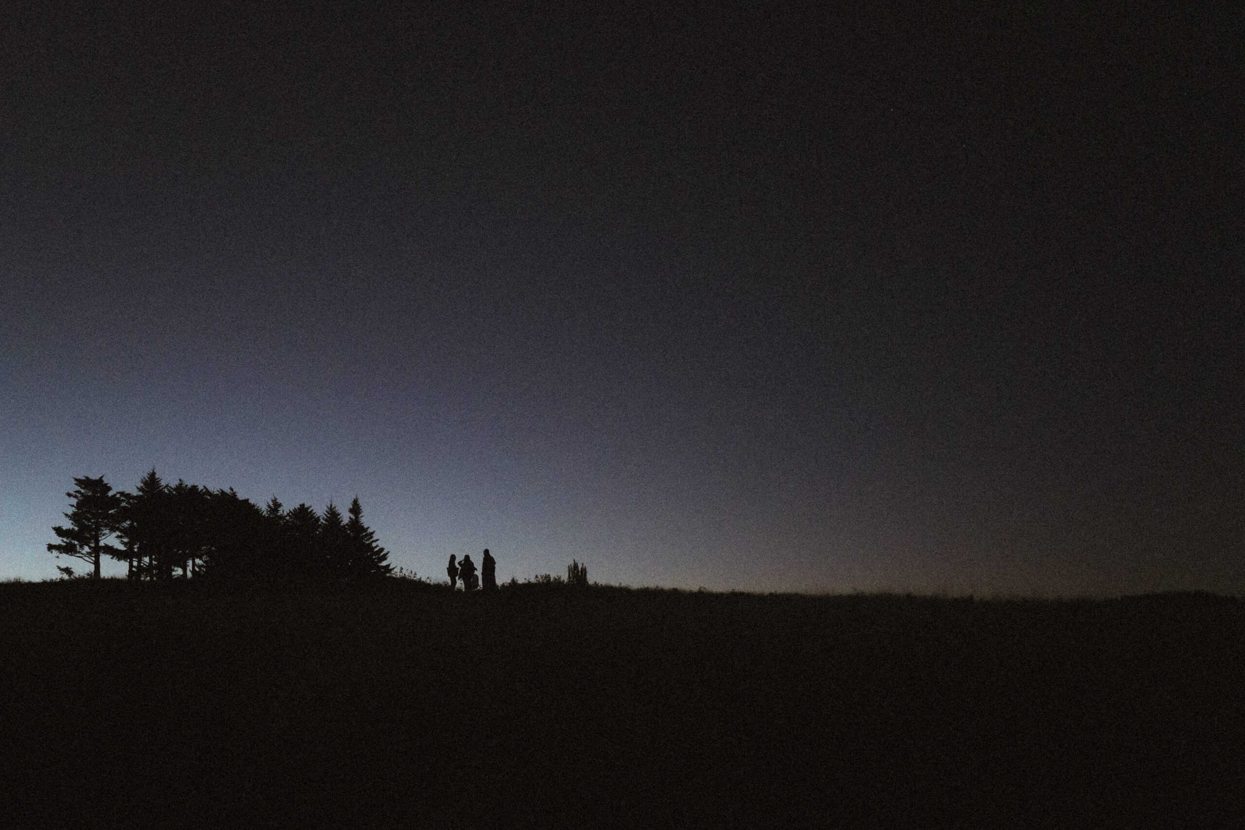 Four people standing in the darkness on a mountaintop waiting for the couple's sunrise mountain hiking elopement