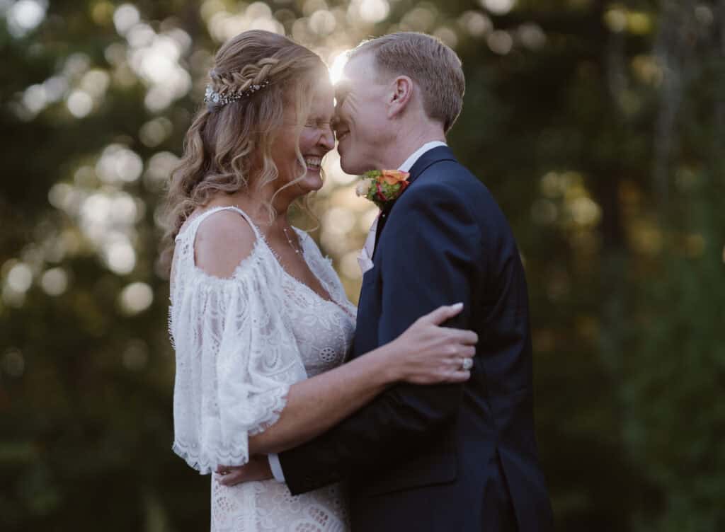 A newlywed couple embracing each other face to face while laughing with the sun backlighting them. 