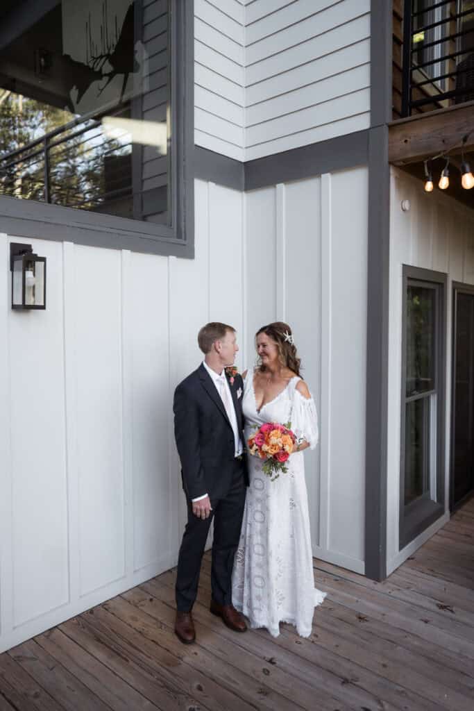 A newlywed couple look lovingly at teach other on a large porch with hanging lights. 