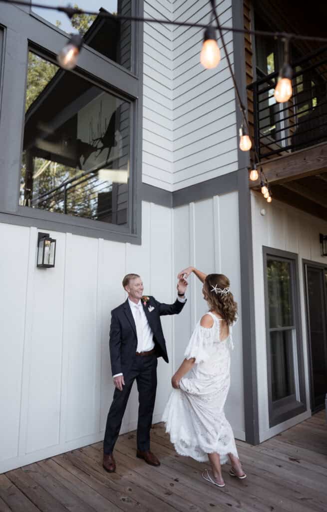 A newlywed couple dancing together on a porch with hanging lights. 