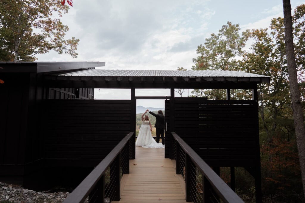 A newlywed couple dance on the porch of their cabin rental in the mountains. 