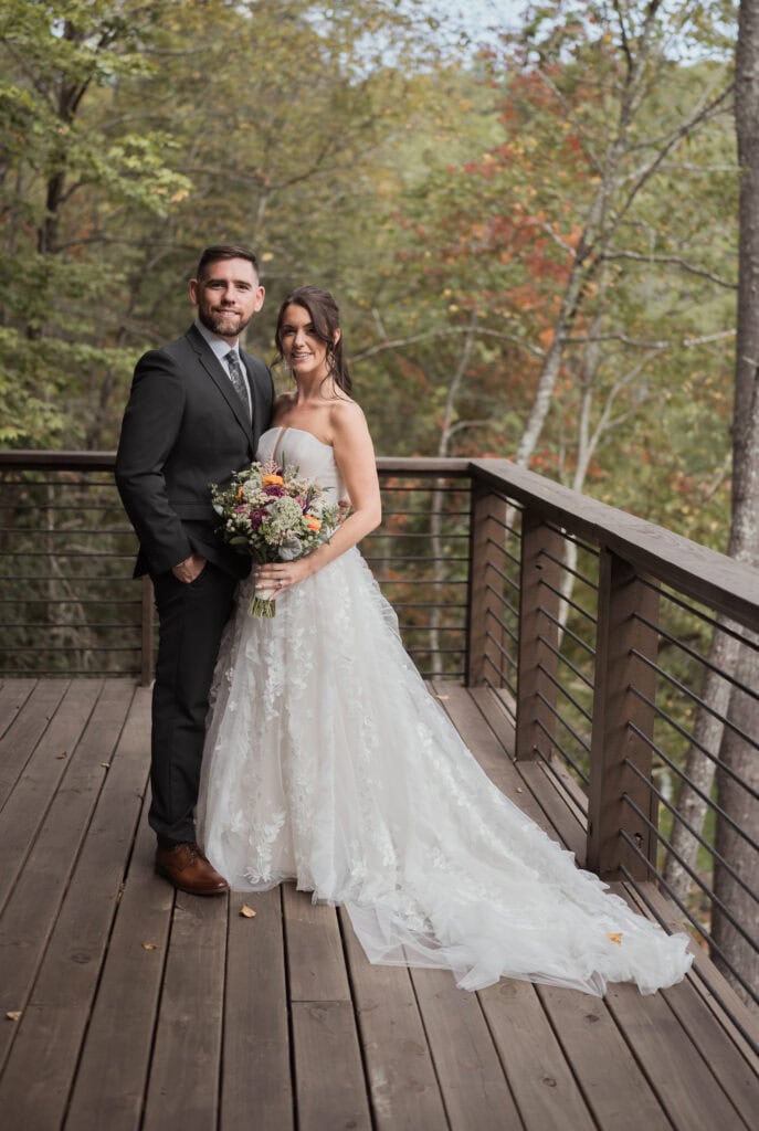 A newlywed couple standing in wedding attire on the porch of their cabin rental. 