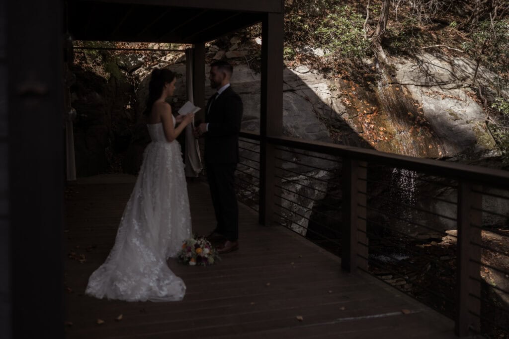 A couple in wedding attire saying their private vows next to a little  waterfall at their cabin rental. 