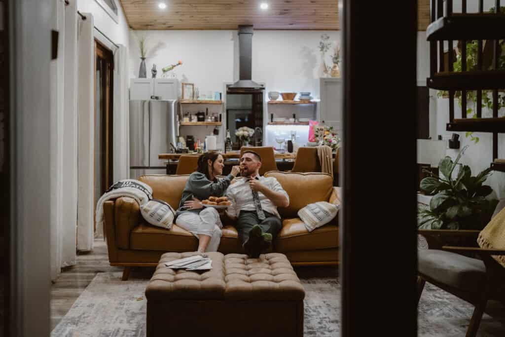 A couple feeding each other doughnuts on the couch. 
