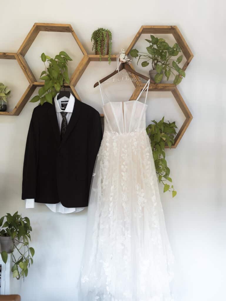 A couple's wedding attire hanging up on the wall with plants. 