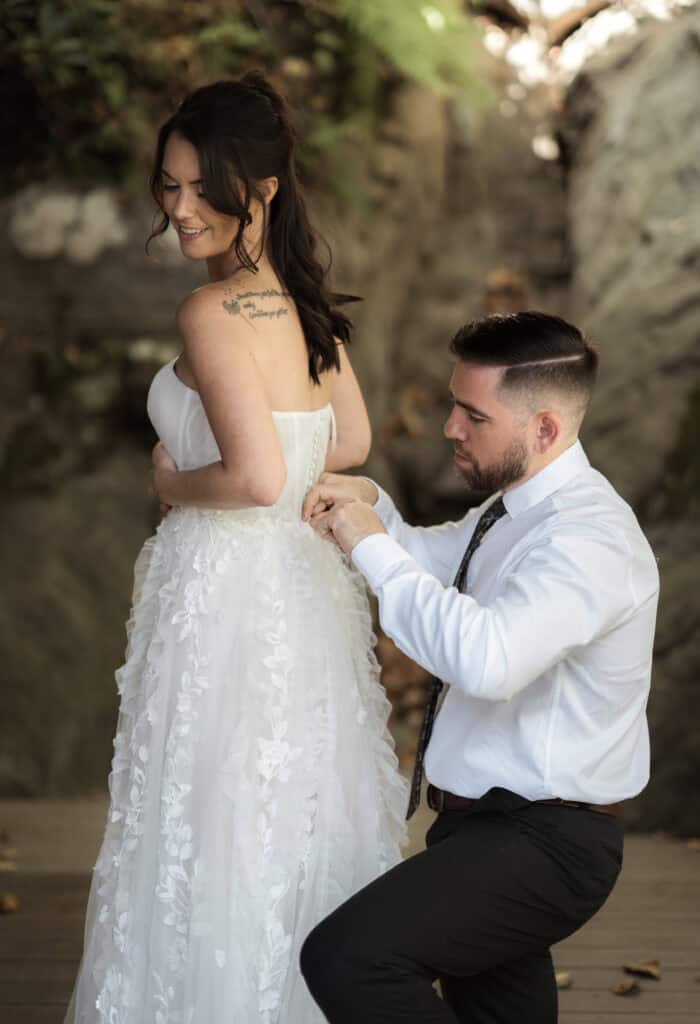 A couple helping each other into wedding attire on their wedding day.