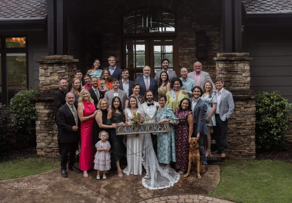 A happily family celebrating the newlyweds in front of a cabin with stone and a black exterior. 