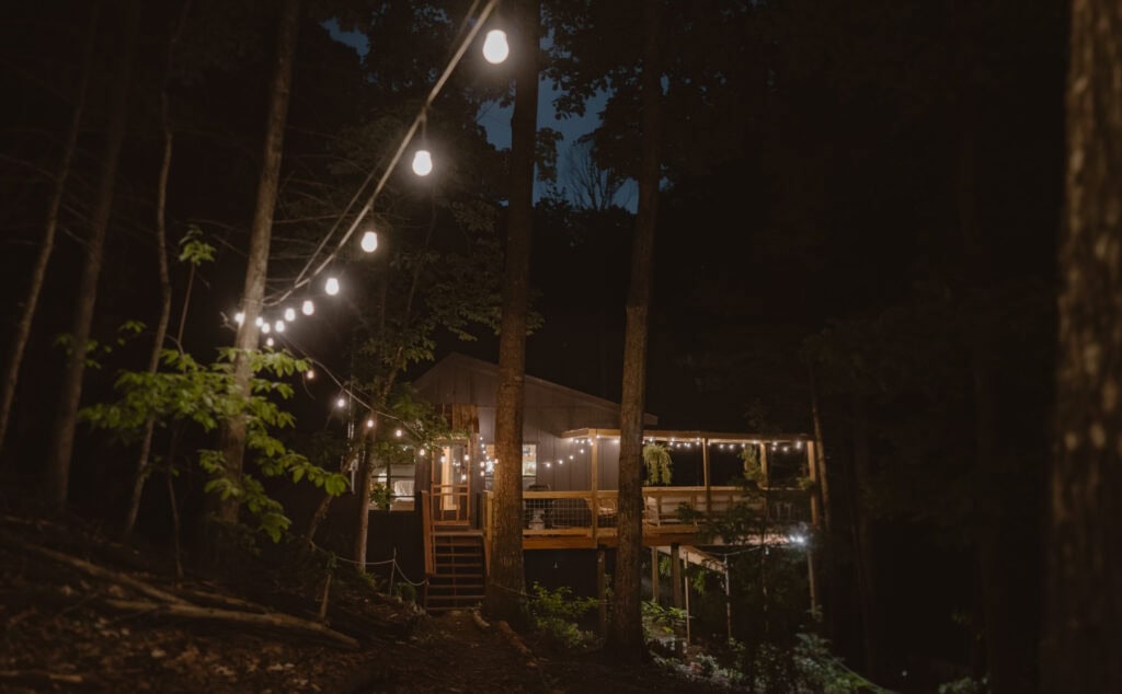 A view of a cabin in the forest with at night with hanging lights.