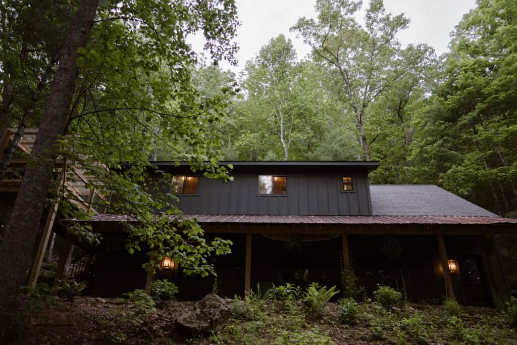 A view of a cabin in the forest with a black exterior. 