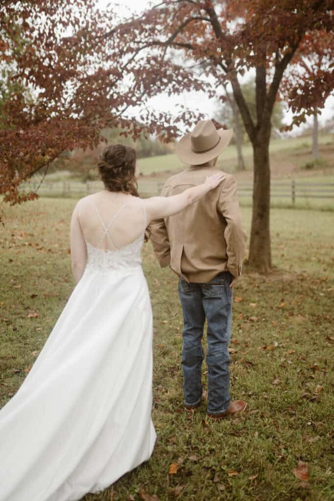 A couple experience their first look in an open field with a tree with red leaves. 