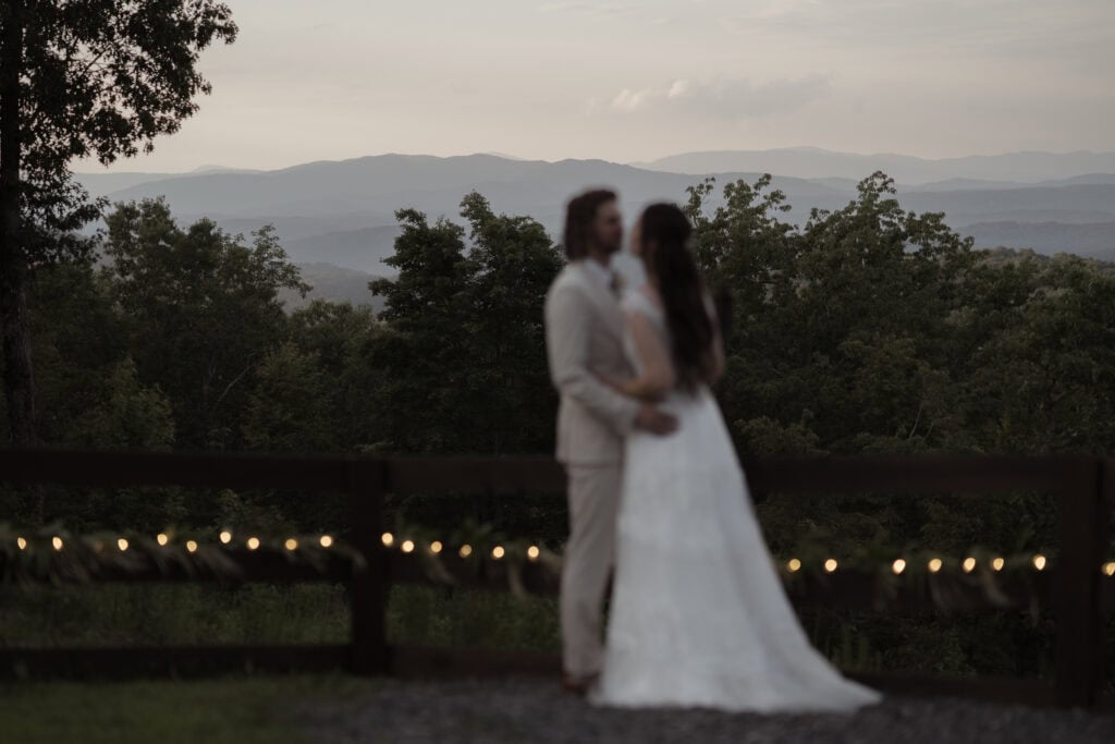A newlywed couple kisses with mountains in the distance. 