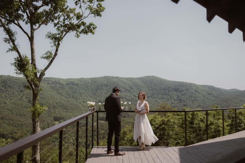 A couple saying their private vows to one another on a large porch overlooking the mountains. 