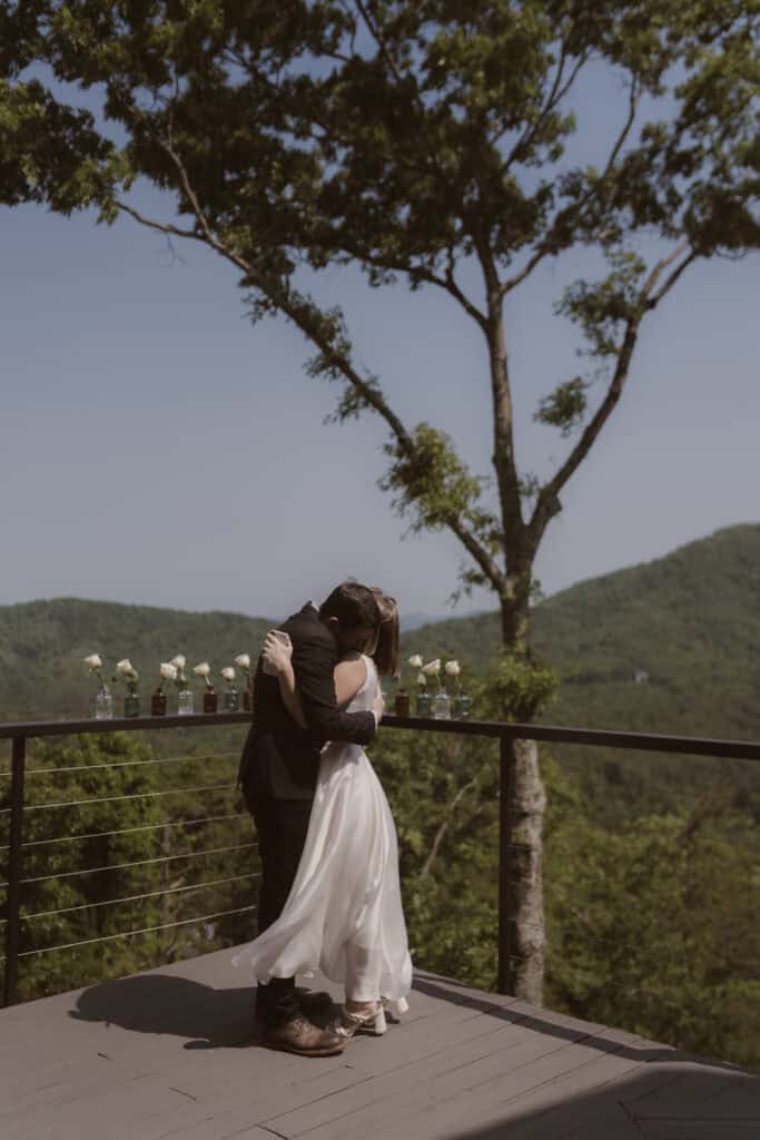 A newlywed couple embracing each other for a hug on a large porch with a mountain view in the distance. 