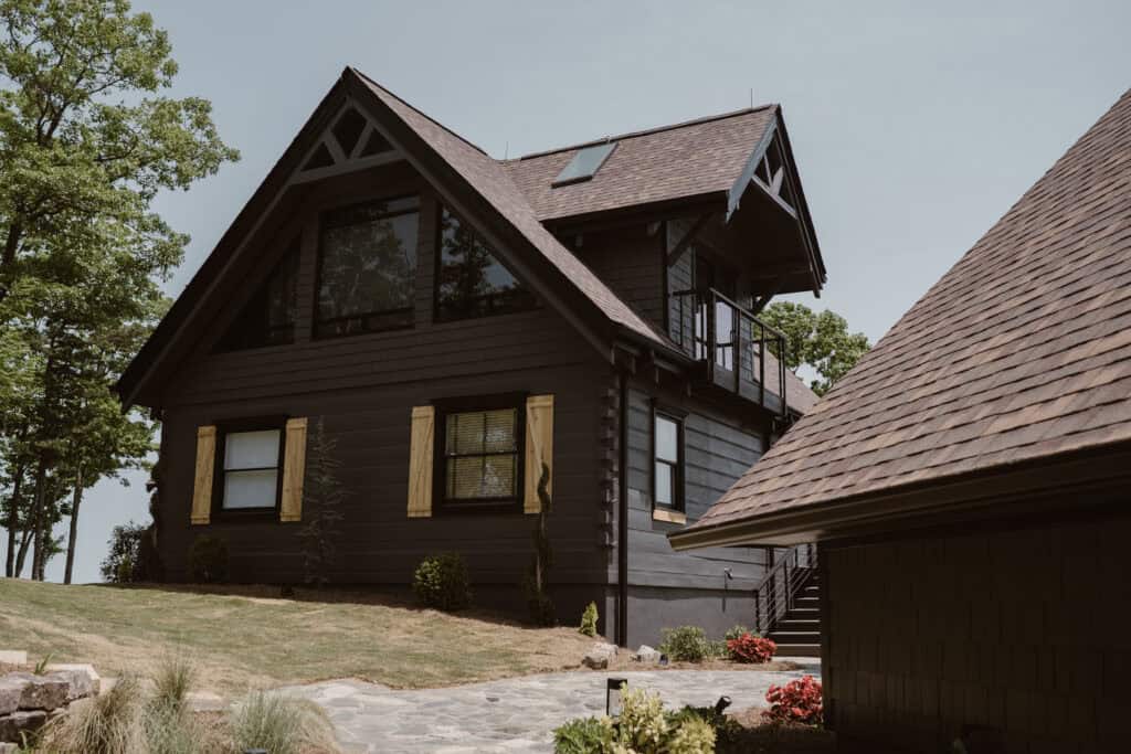 A photo of an Airbnb with black exterior and yellow shutters surrounded by trees. 