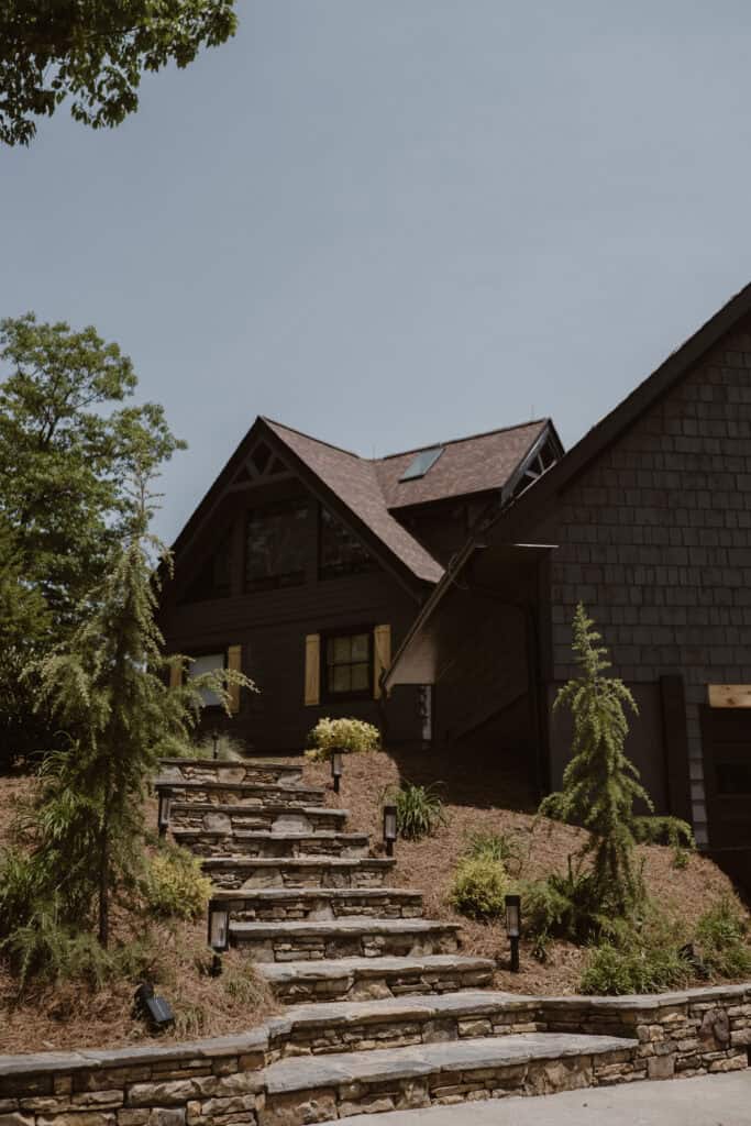 A photo of an Airbnb with black exterior, yellow shutters, and stone steps leading to the door. 